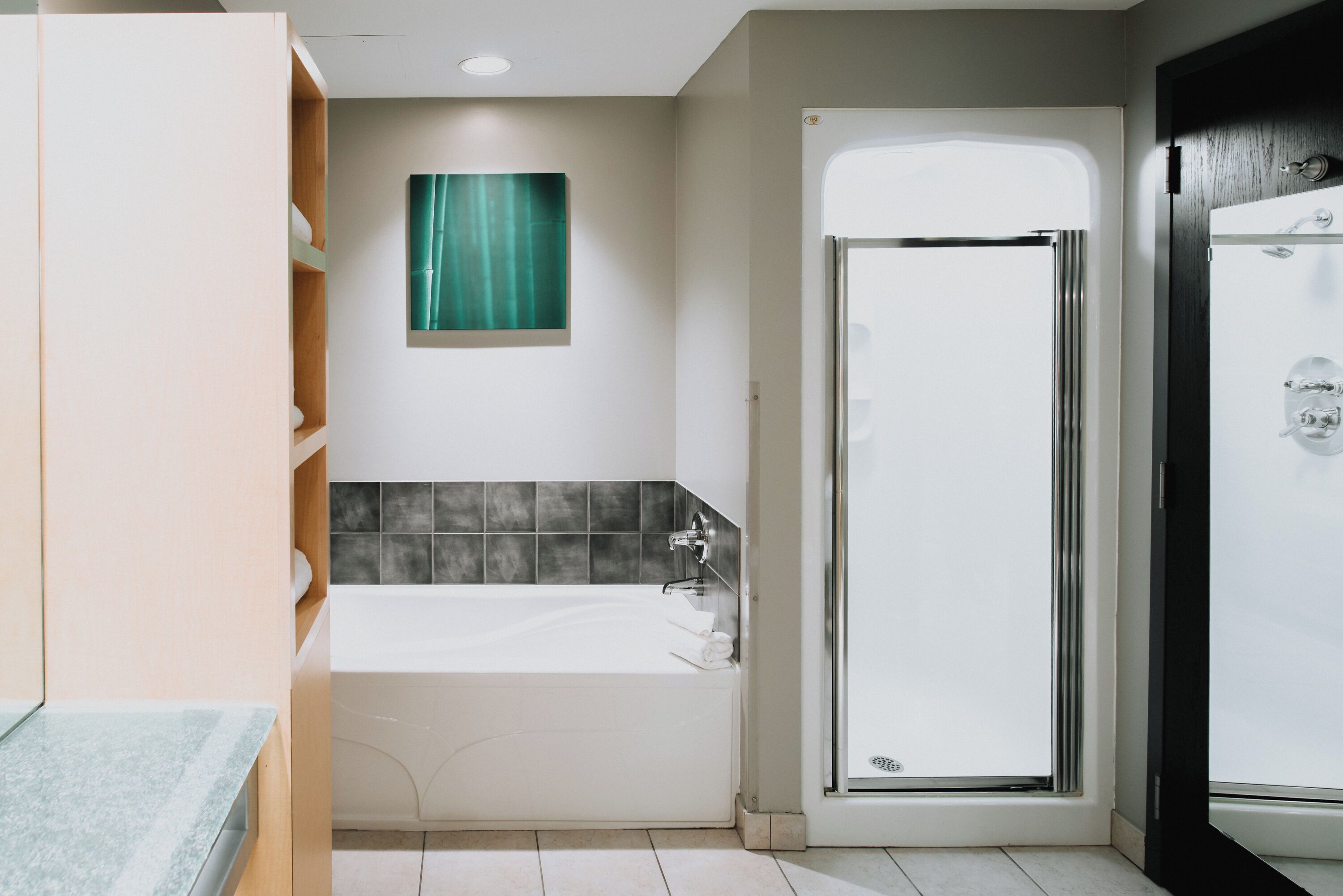 Un baño moderno con bañera, cabina de ducha de vidrio y un cuadro abstracto verde en la pared.