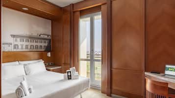 Habitación de hotel con cama, escritorio, computadora portátil y vista de edificios a través de un ventanal.