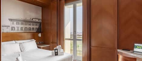 Habitación de hotel con cama, escritorio, computadora portátil y vista de edificios a través de un ventanal.