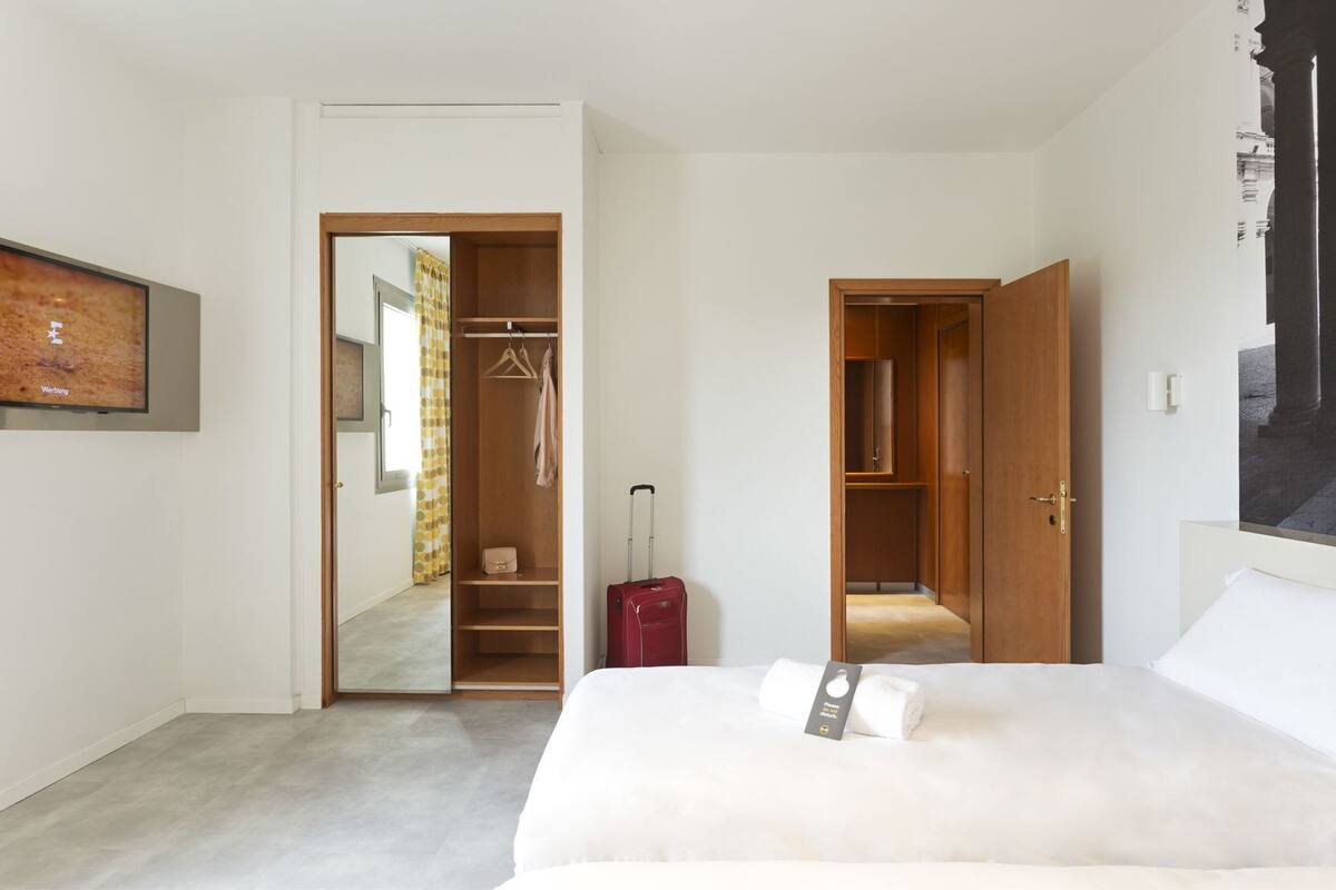 Quarto de hotel com cama, guarda-roupa, espelho e televisão.