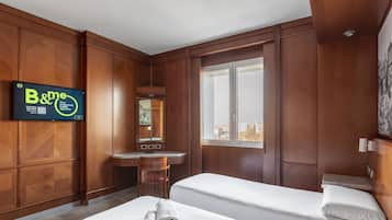 A hotel room with two beds, a desk, a mirror, and a large window.