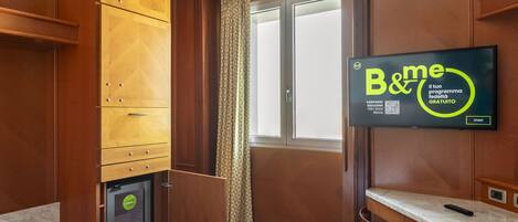 Habitación de hotel con armarios de madera, encimera de mármol, televisión mostrando un programa y una ventana con cortinas.