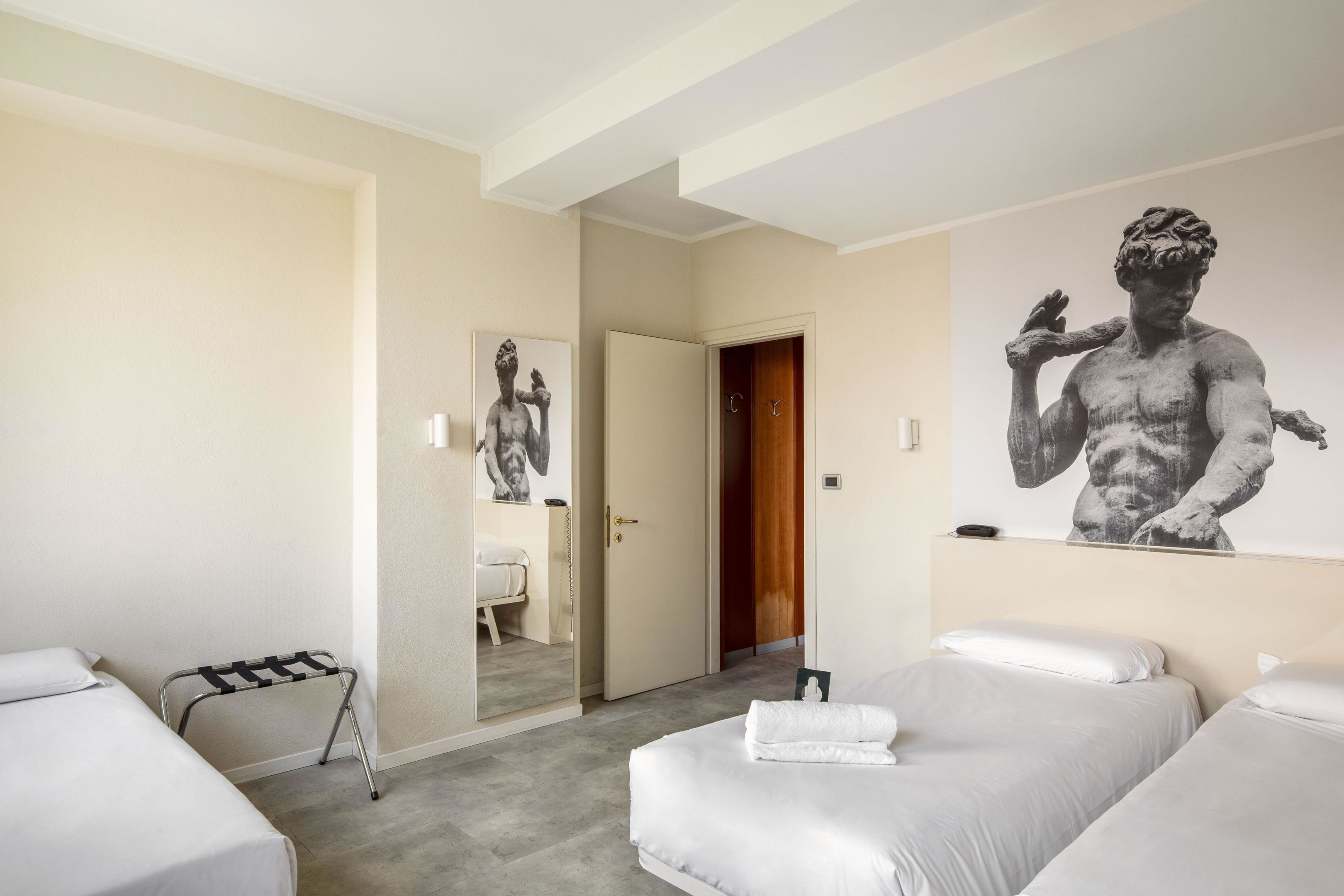A hotel room with two beds, a mirror, a statue, and a door leading to a bathroom.