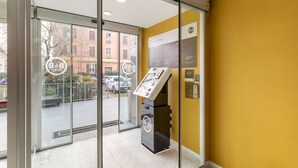 L’entrée d’un hôtel avec une porte en verre, un comptoir d’accueil et un mur jaune.