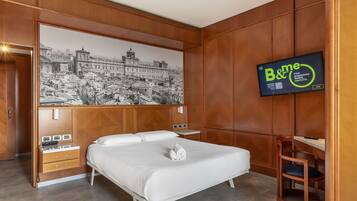A hotel room with a large bed, a wooden wardrobe, a desk, and a television displaying a program.