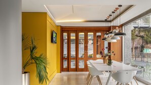 Un espace de salle à manger moderne avec un mur d’accent jaune, une grande fenêtre offrant une belle vue et une table blanche avec des chaises.