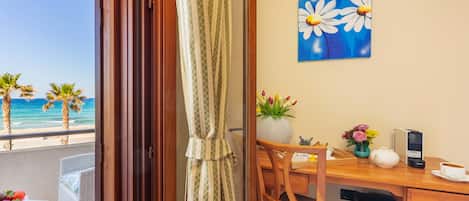 Un balcon donnant sur la plage, un bureau en bois orné d’un vase de fleurs, une théière et une machine à café.