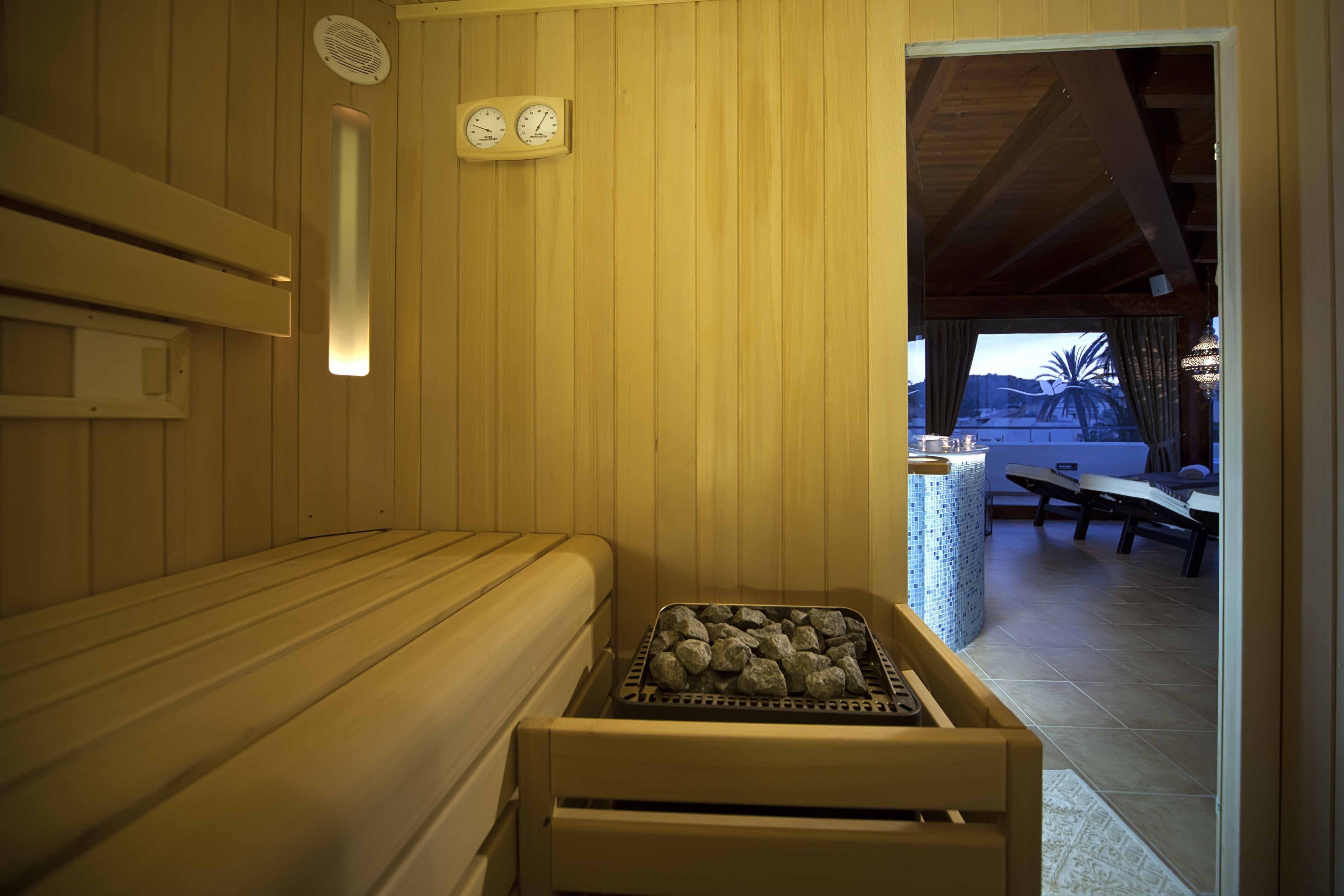 A sauna room with wooden walls, a bench, a tray of rocks, and a clock on the wall.