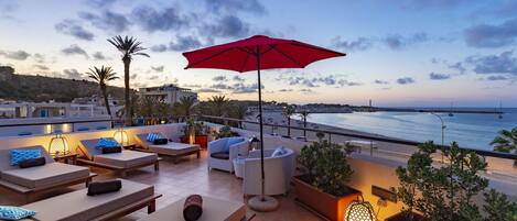 A rooftop terrace with lounge chairs, a red umbrella, and potted plants.
