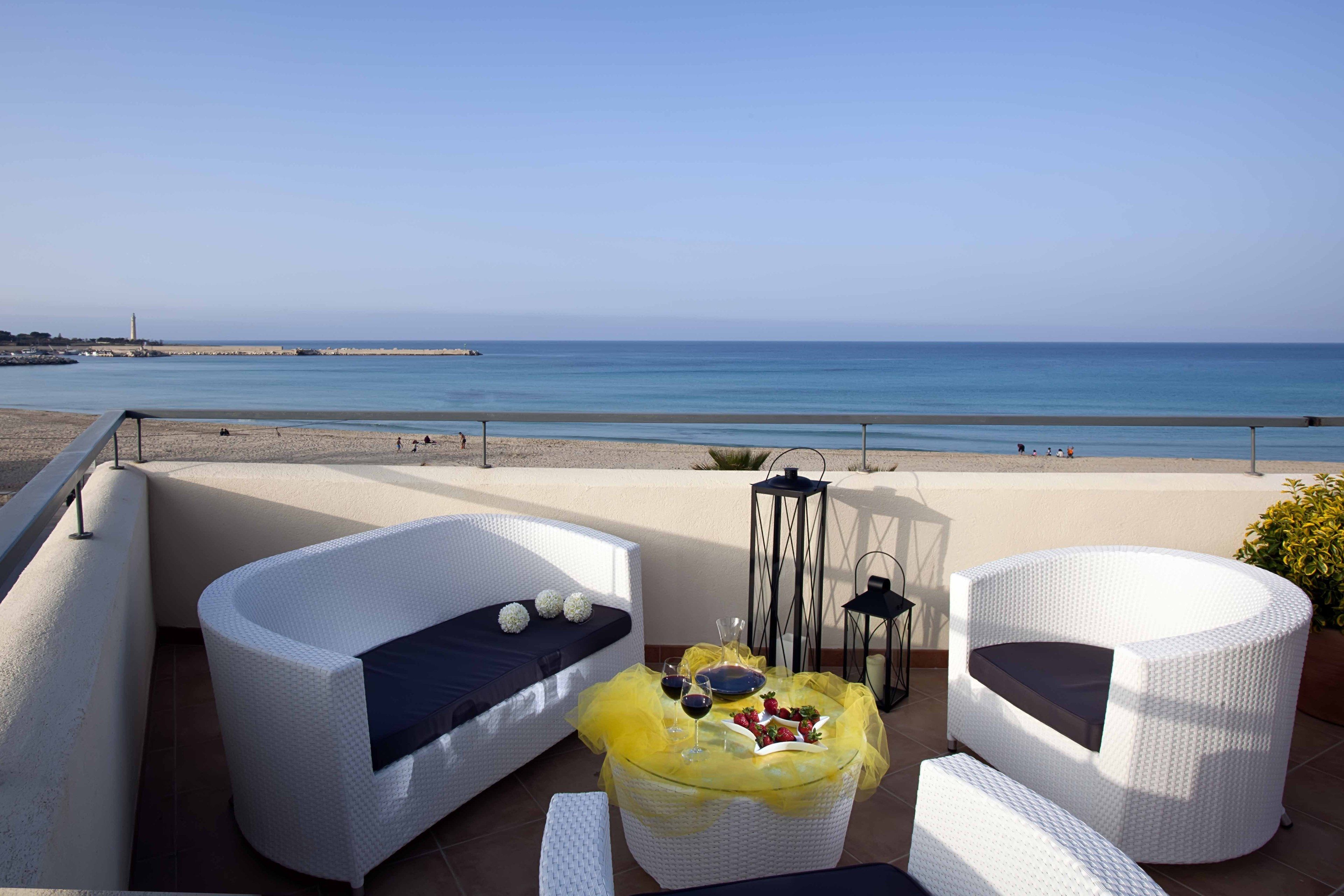 A balcony with white wicker furniture, a glass table with a yellow cover, and a view of the sea.