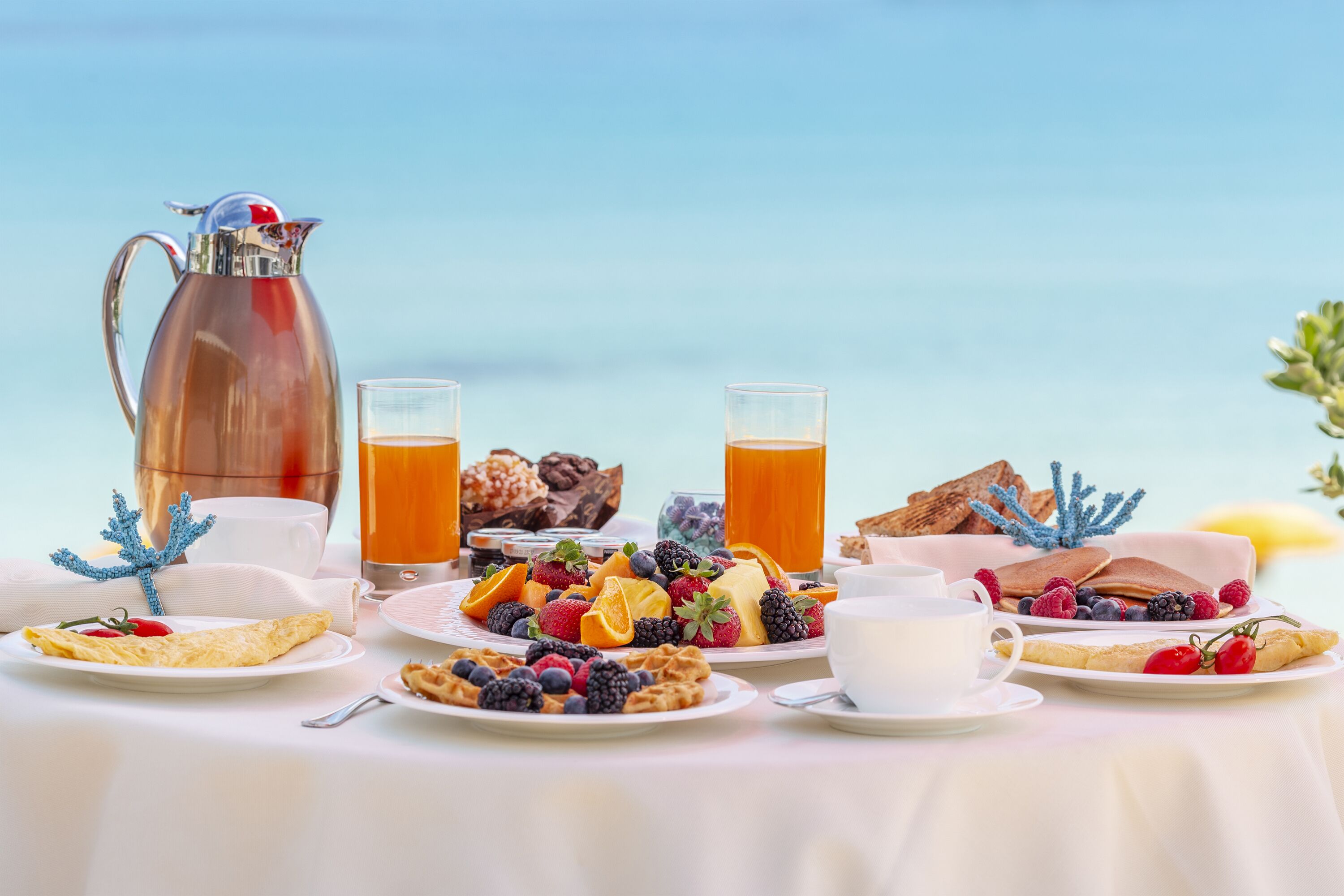 A breakfast table with various dishes, a pitcher, and glasses of orange juice.