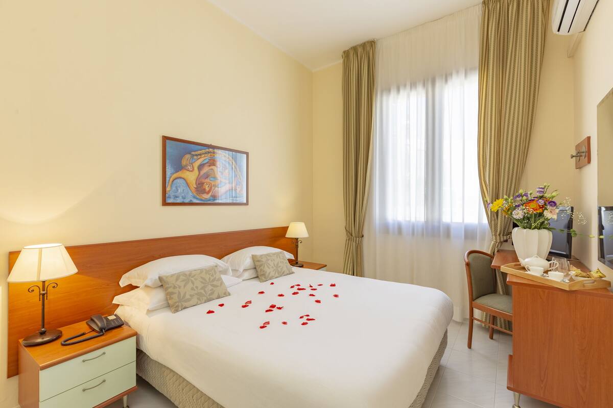 Een hotelkamer met een groot bed, een bureau met stoel, een telefoon en een schilderij aan de muur.