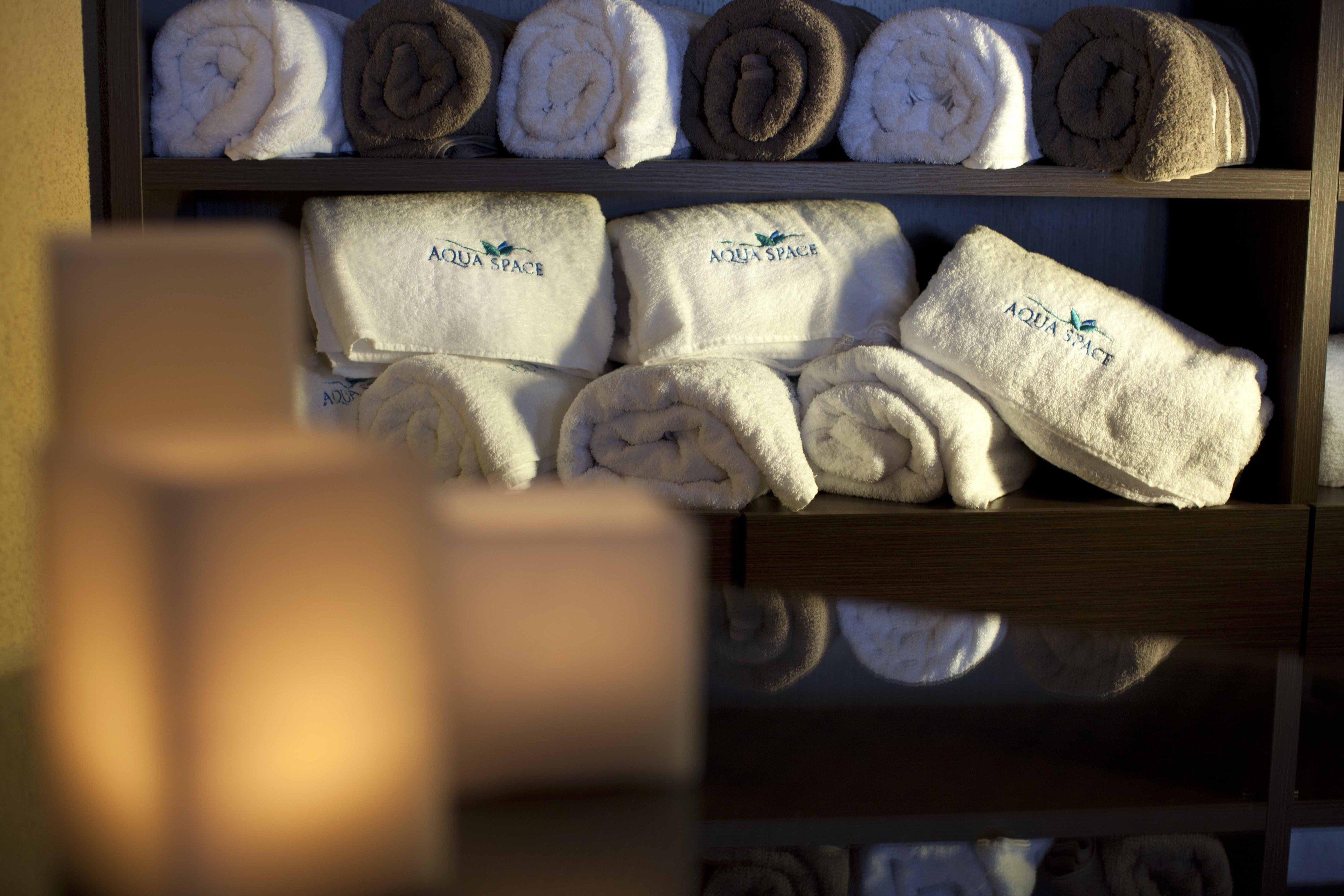 A shelf with neatly rolled towels in various colors, some with 'Aqua Space' branding.