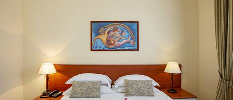 A hotel room with a bed, two bedside tables with lamps, a painting on the wall, and rose petals on the bed.