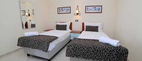 Habitación de hotel con dos camas, un espejo grande, luces empotradas en la pared y cuadros enmarcados.