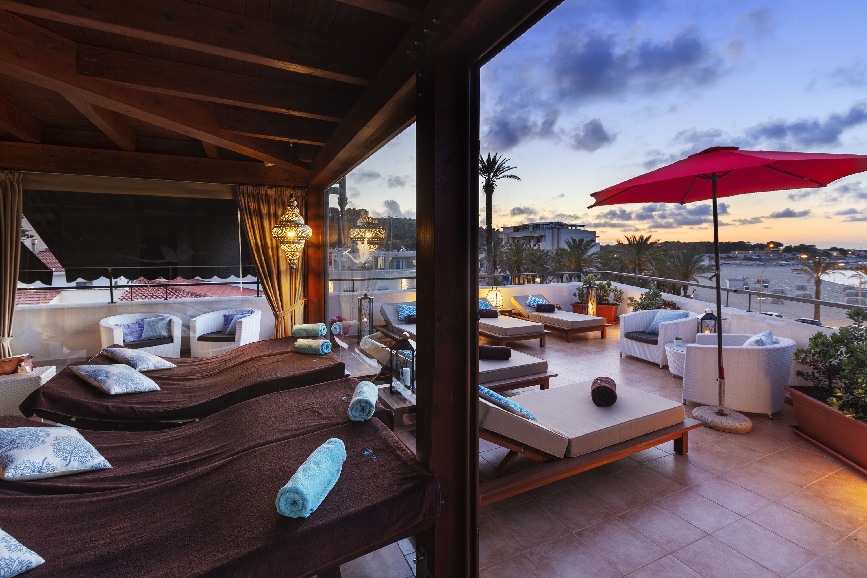 A rooftop terrace with sun loungers, a red umbrella, and a view of the marina.
