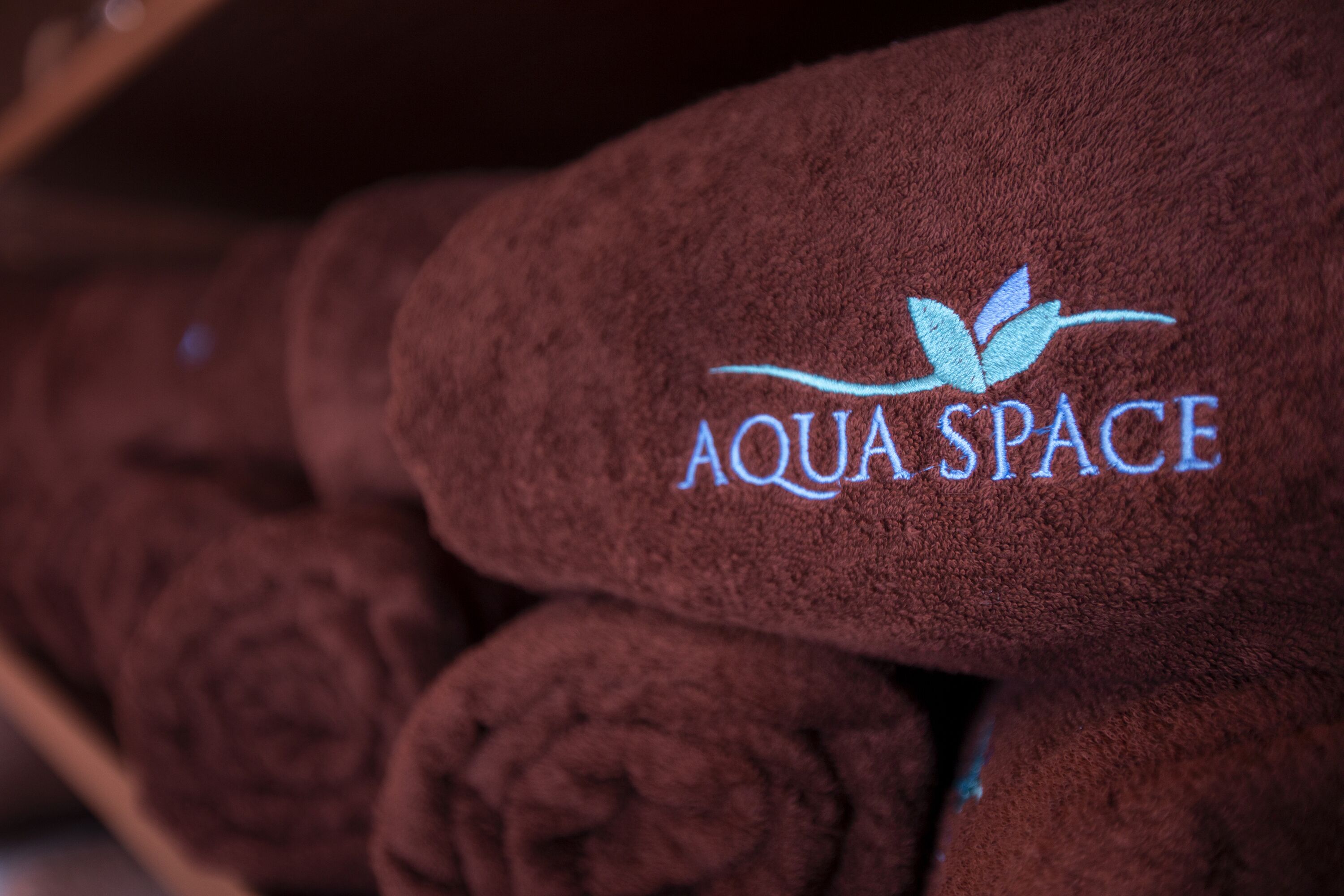 A stack of brown towels with the logo "AQUA SPACE" embroidered on them.