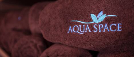 A stack of brown towels with the logo "AQUA SPACE" embroidered on them.
