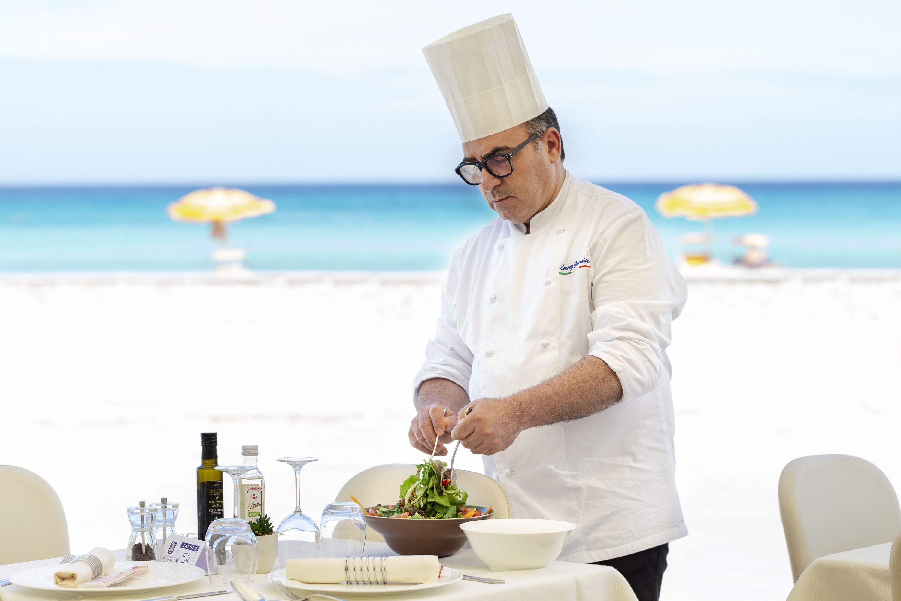 A chef preparing food at a table with a view of the beach.