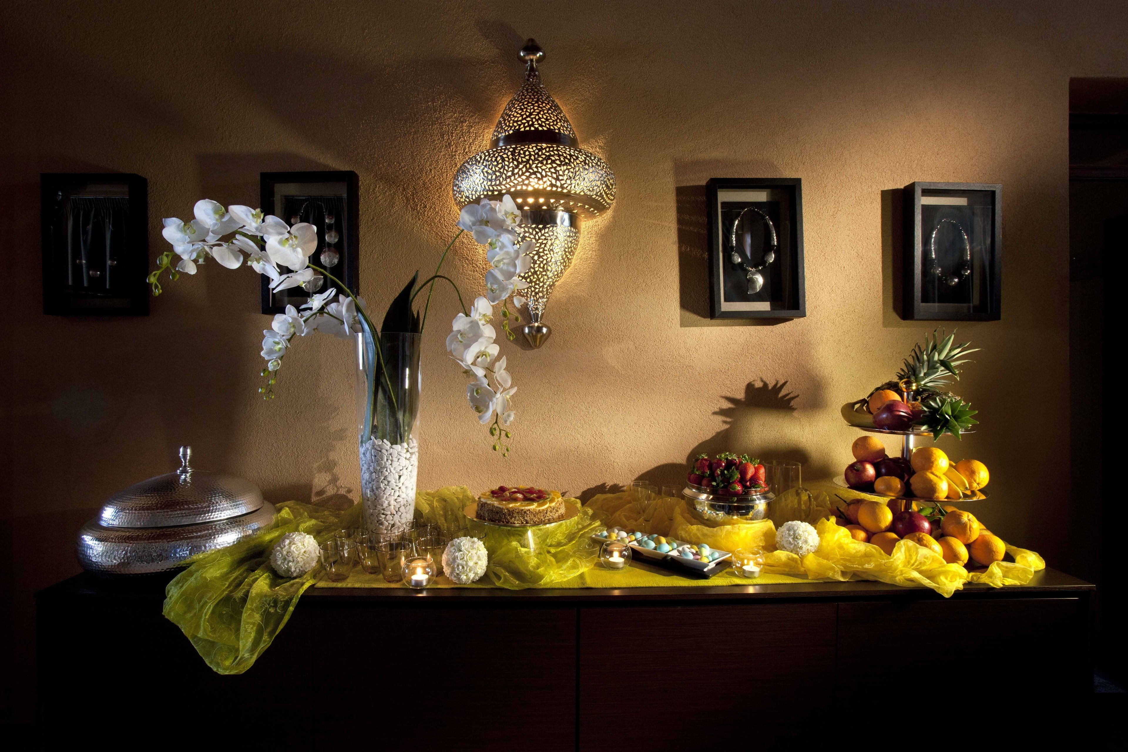 A table with a decorative lamp, framed pictures, and a fruit arrangement.