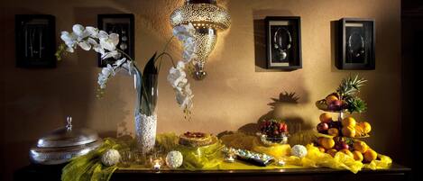 A table with a decorative lamp, framed pictures, and a fruit arrangement.