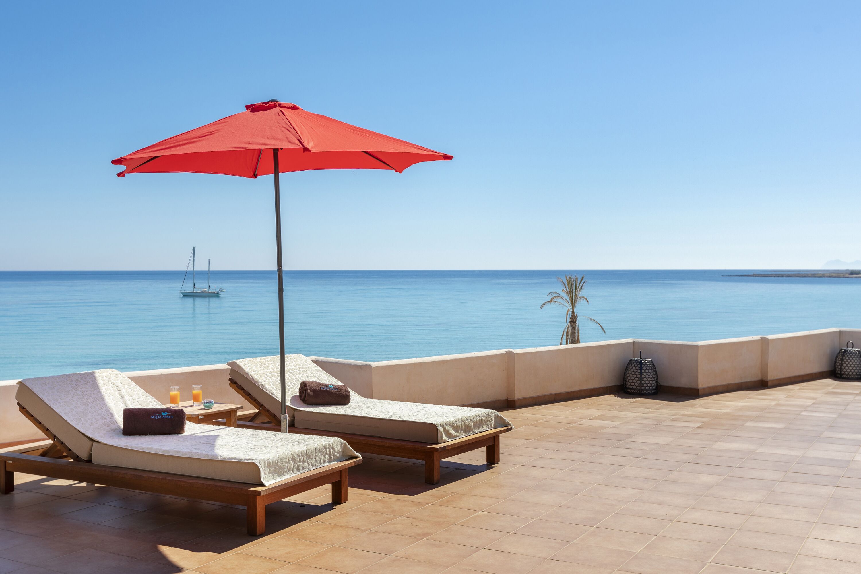 Una terraza con dos sillones, una sombrilla roja y vistas al mar.