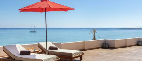 A terrace with two lounge chairs, a red umbrella, and a view of the sea.