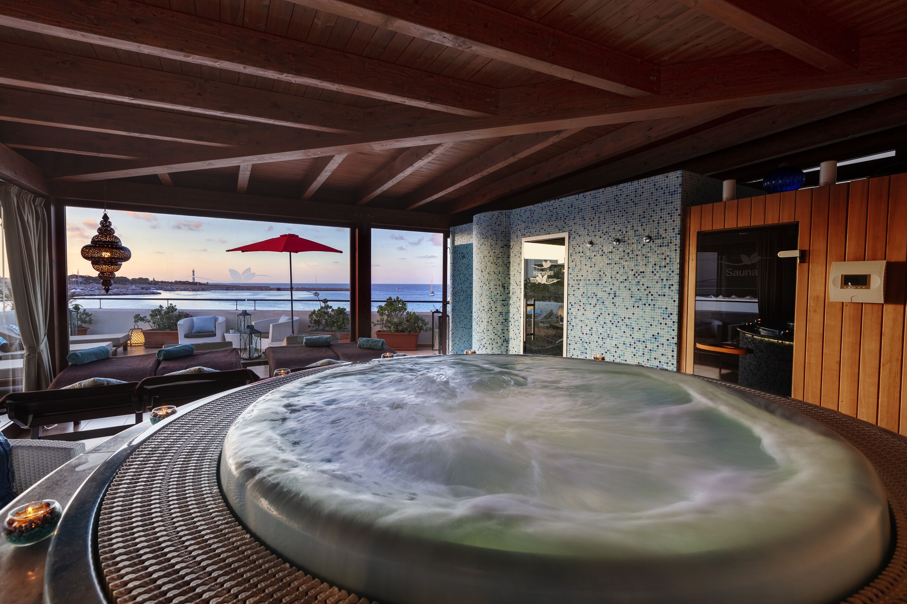 A hot tub with a view of the sea, wooden ceiling beams, and a red umbrella.