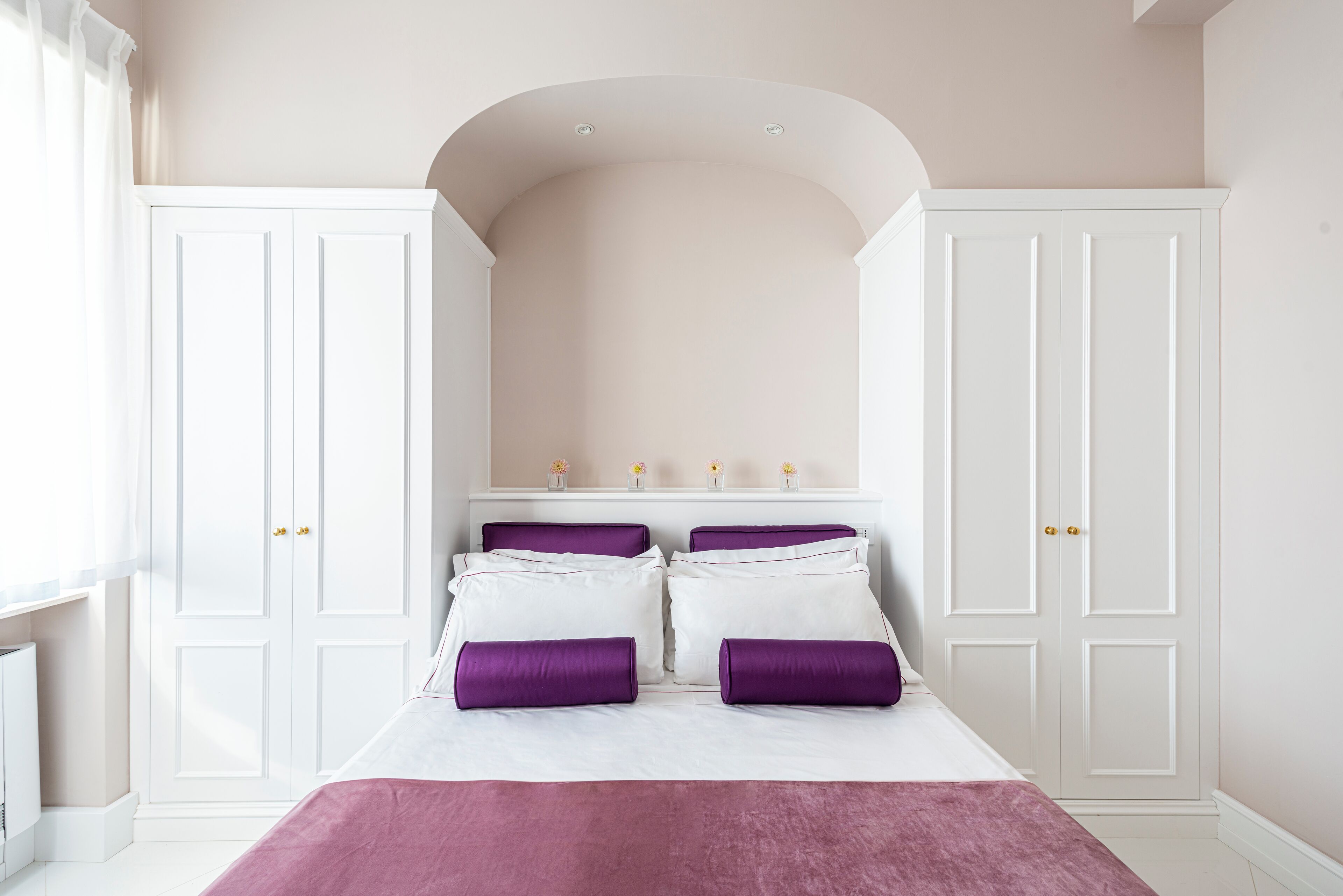 A bedroom with a bed, white wardrobe, and a white arched ceiling.