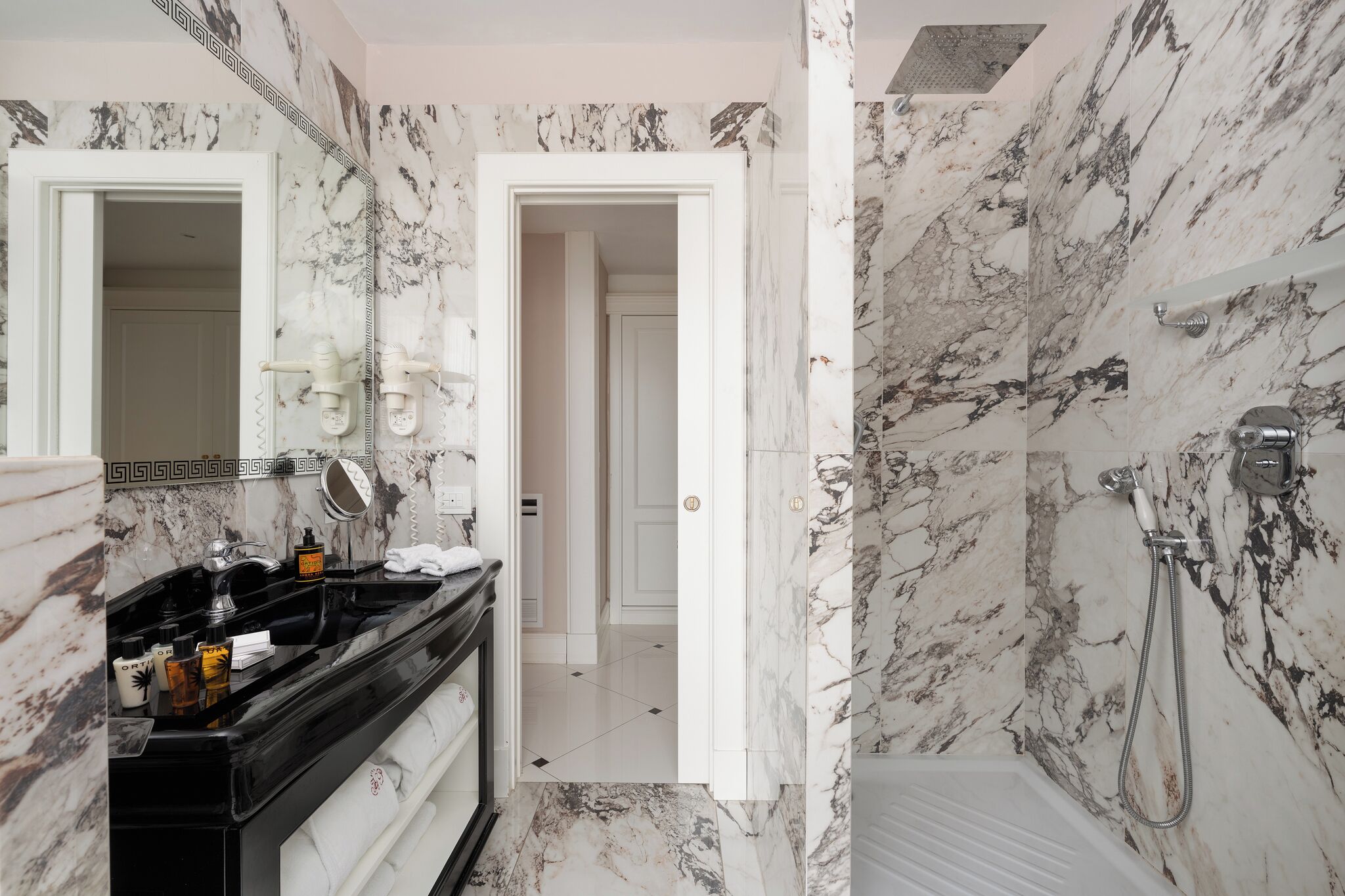 A bathroom with a marble wall, a black vanity, a shower, and a mirror.