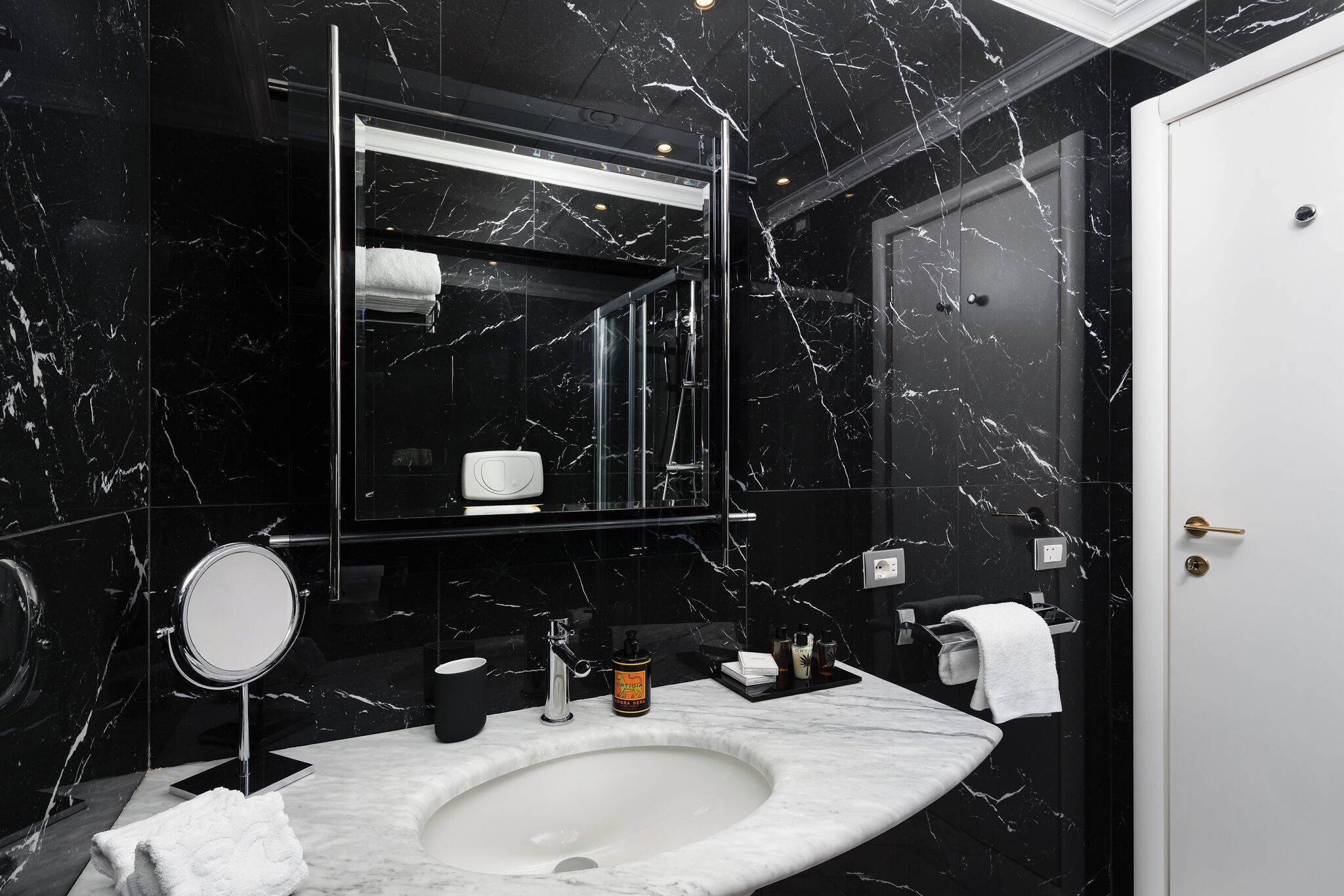 Un baño moderno con un lavabo de mármol, un espejo redondo y un espejo grande sobre el lavabo.
