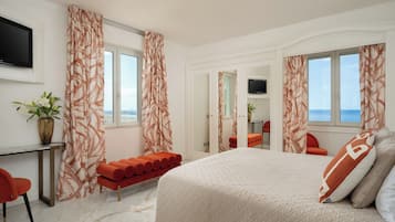 Habitación de hotel con cama, escritorio, silla, banco, televisor y vista al mar.