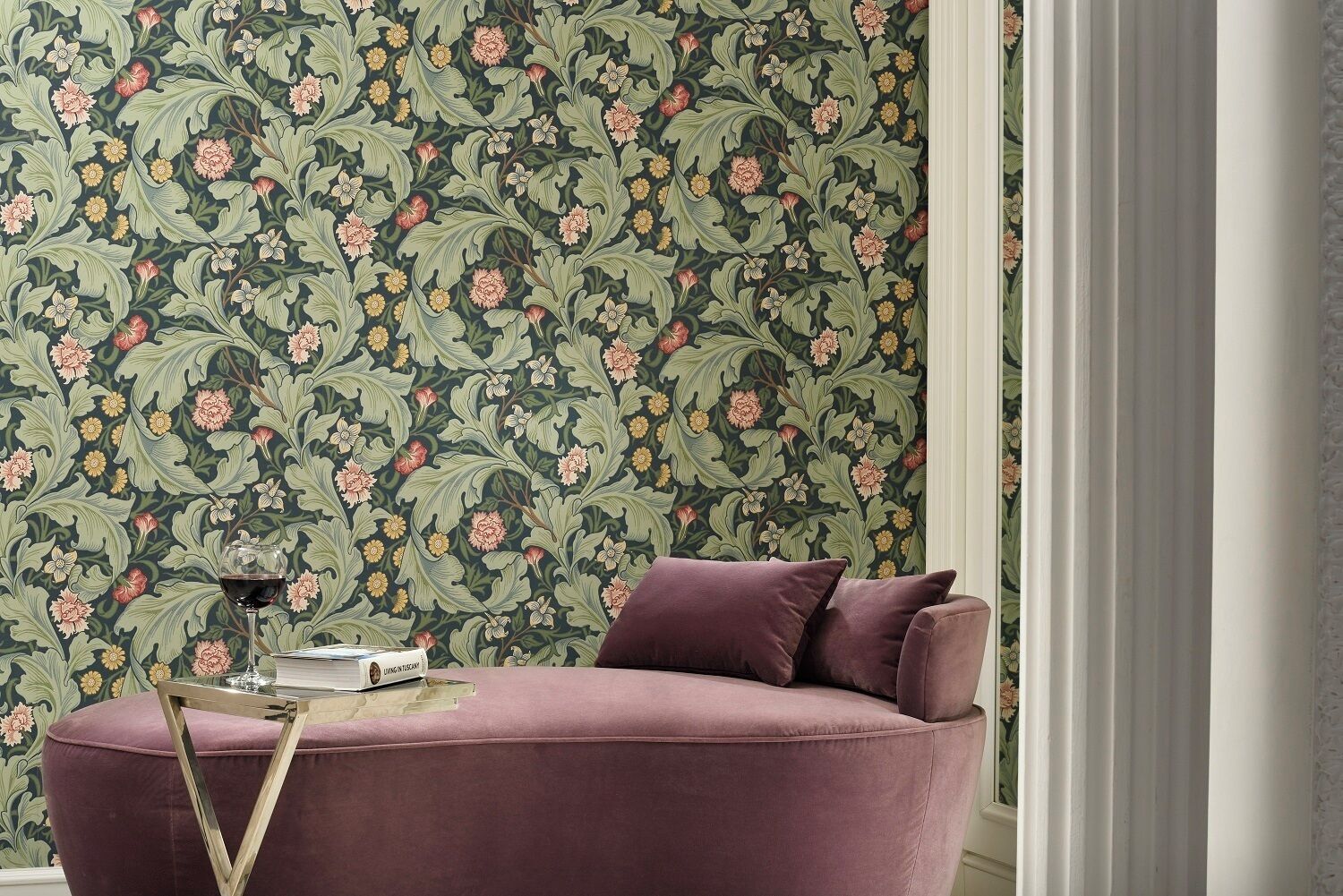 Una habitación con papel tapiz floral, un sofá morado y una copa de vino sobre una mesita auxiliar.