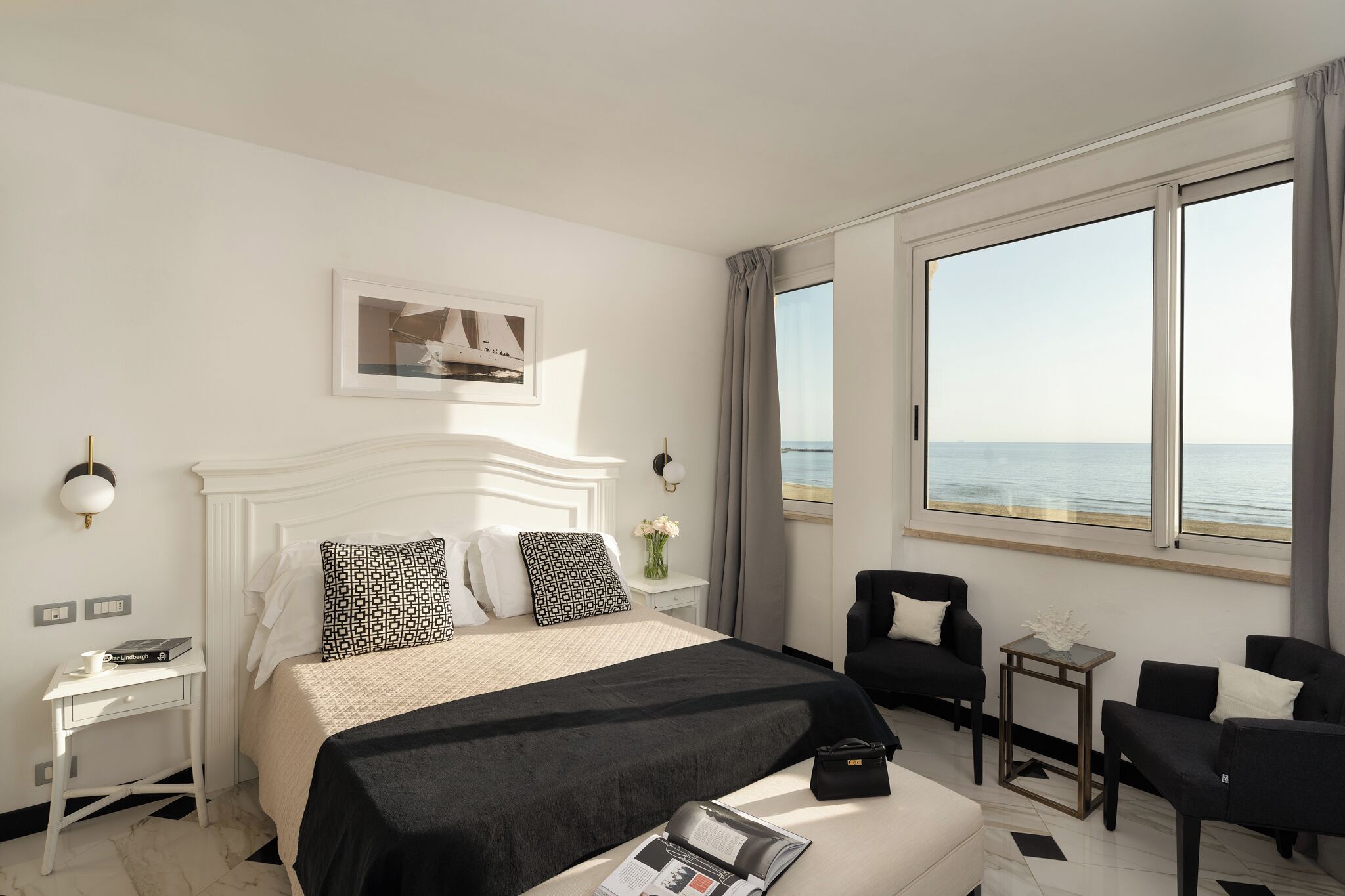 A hotel room with a bed, a desk, a chair, a small table, and a large window with a view.