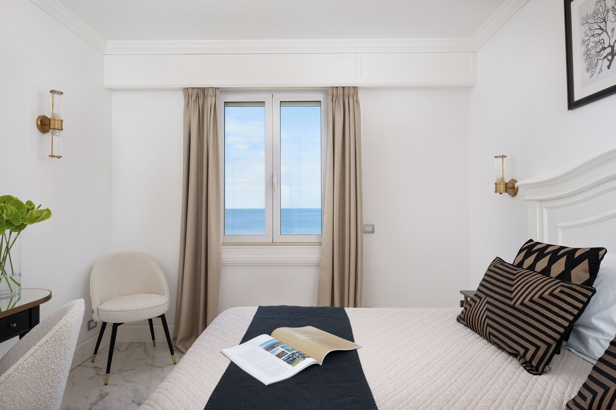 A hotel room with a bed, a chair, a window with curtains, and a view of the sea.
