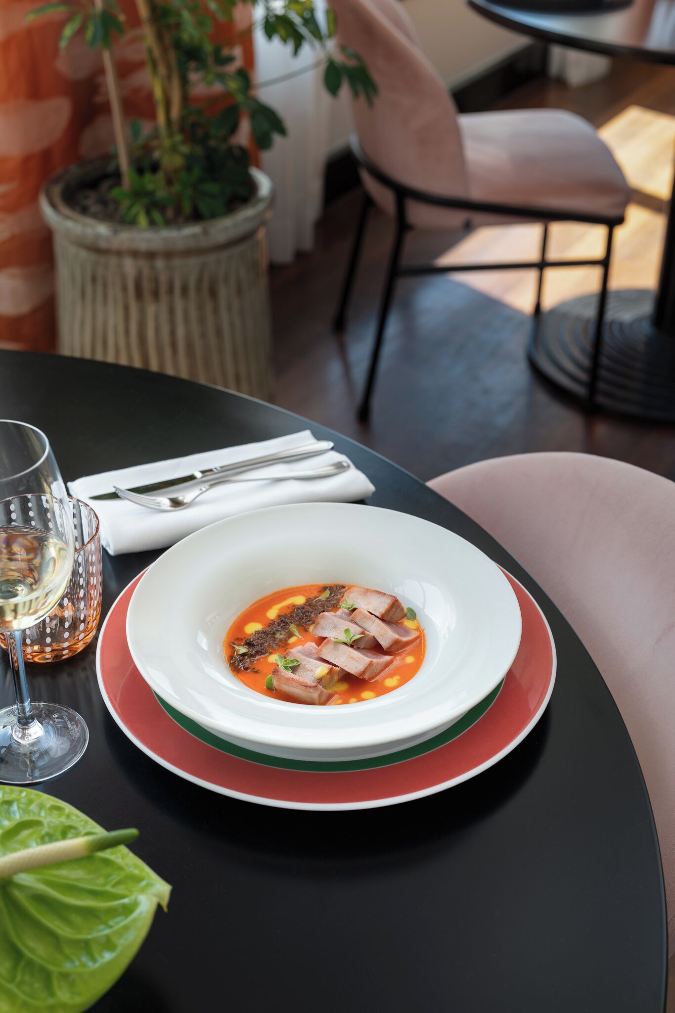 Una mesa con un tazón de sopa, una copa de vino y una planta en maceta.