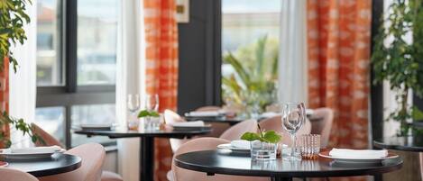 A dining area with round tables, chairs, and a view of the city through large windows.