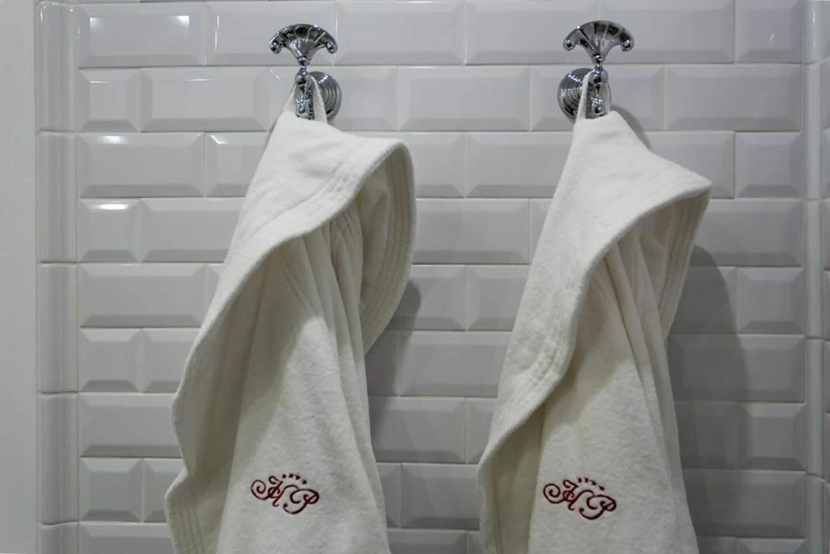 Two white towels hanging on a white tiled wall.