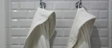 Two white towels hanging on a white tiled wall.