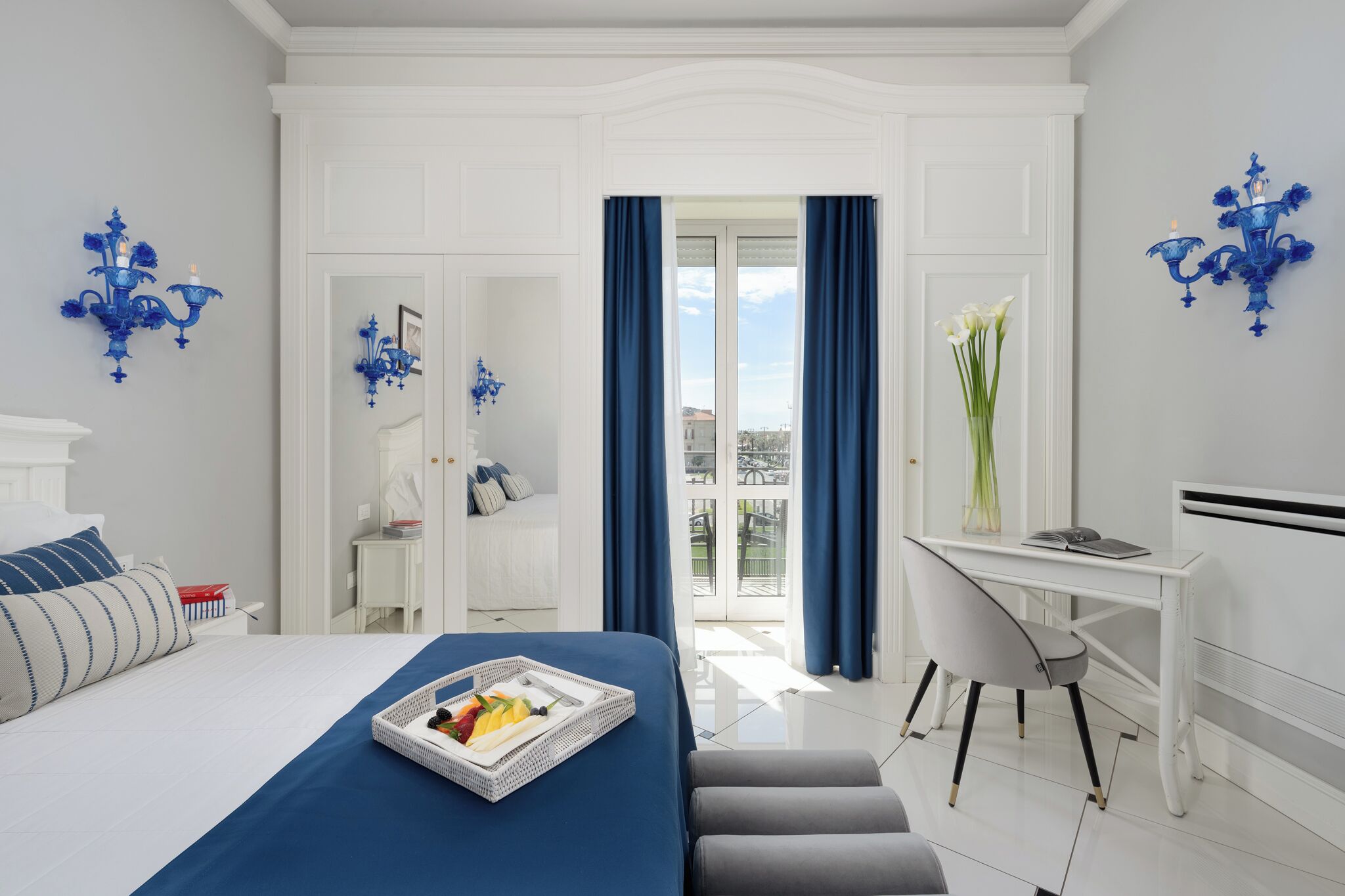 A hotel room with a bed, a desk, a chair, a window with curtains, and a balcony.