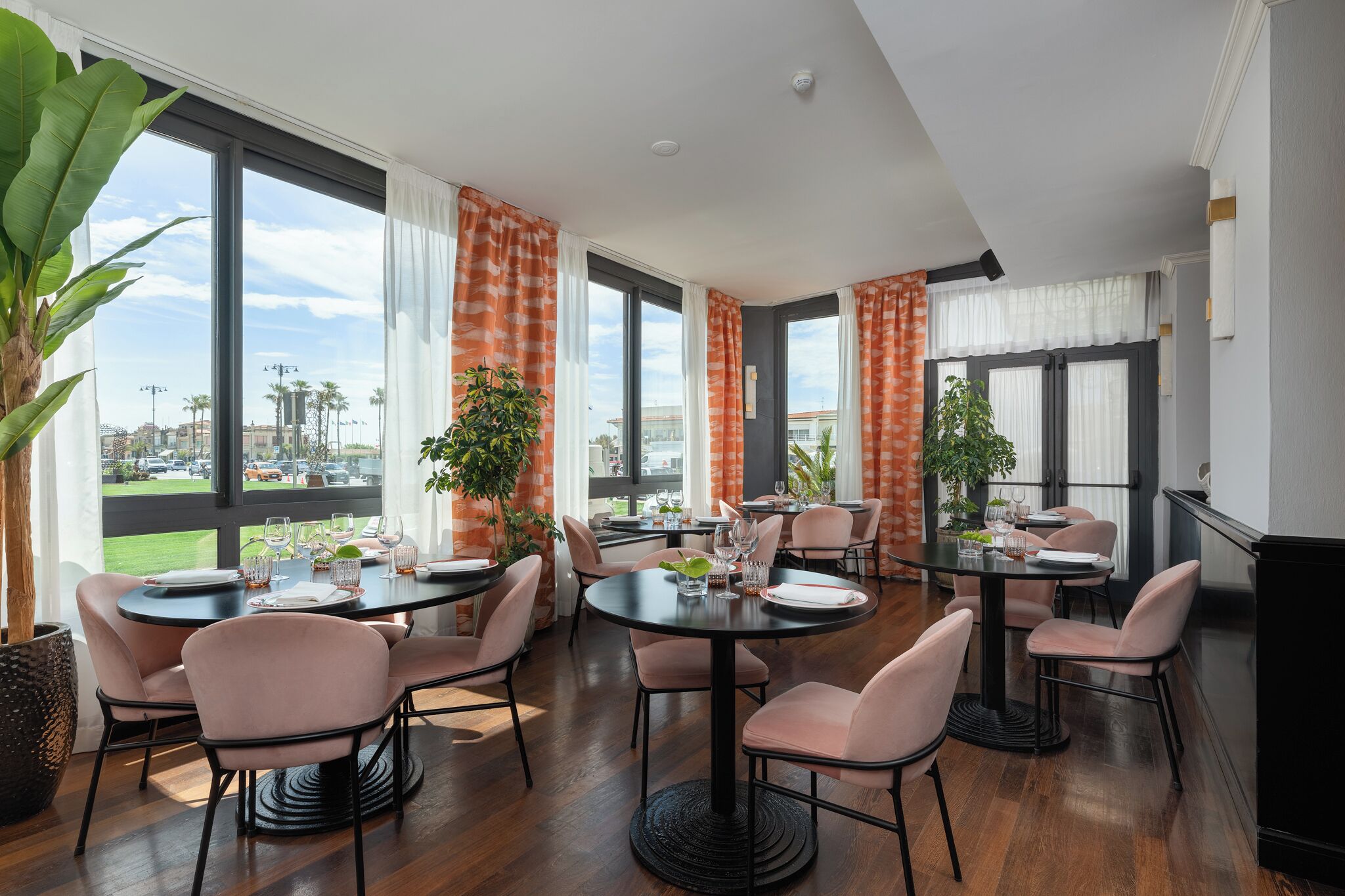 Un espace repas moderne avec des tables rondes, des chaises roses et de grandes fenêtres donnant sur la ville.