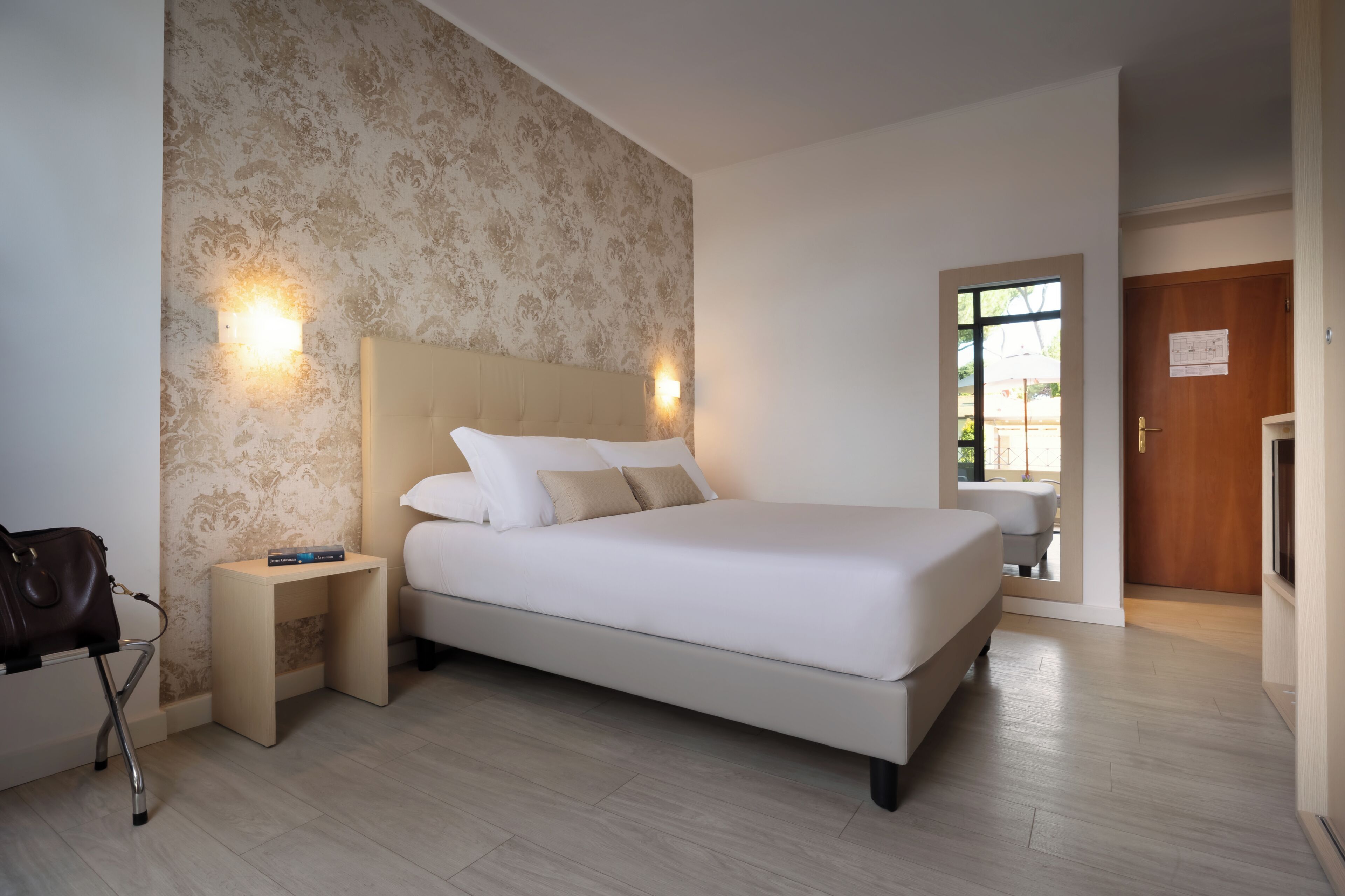 A modern bedroom with a large bed, bedside tables, a nightstand, and a door leading to a balcony.