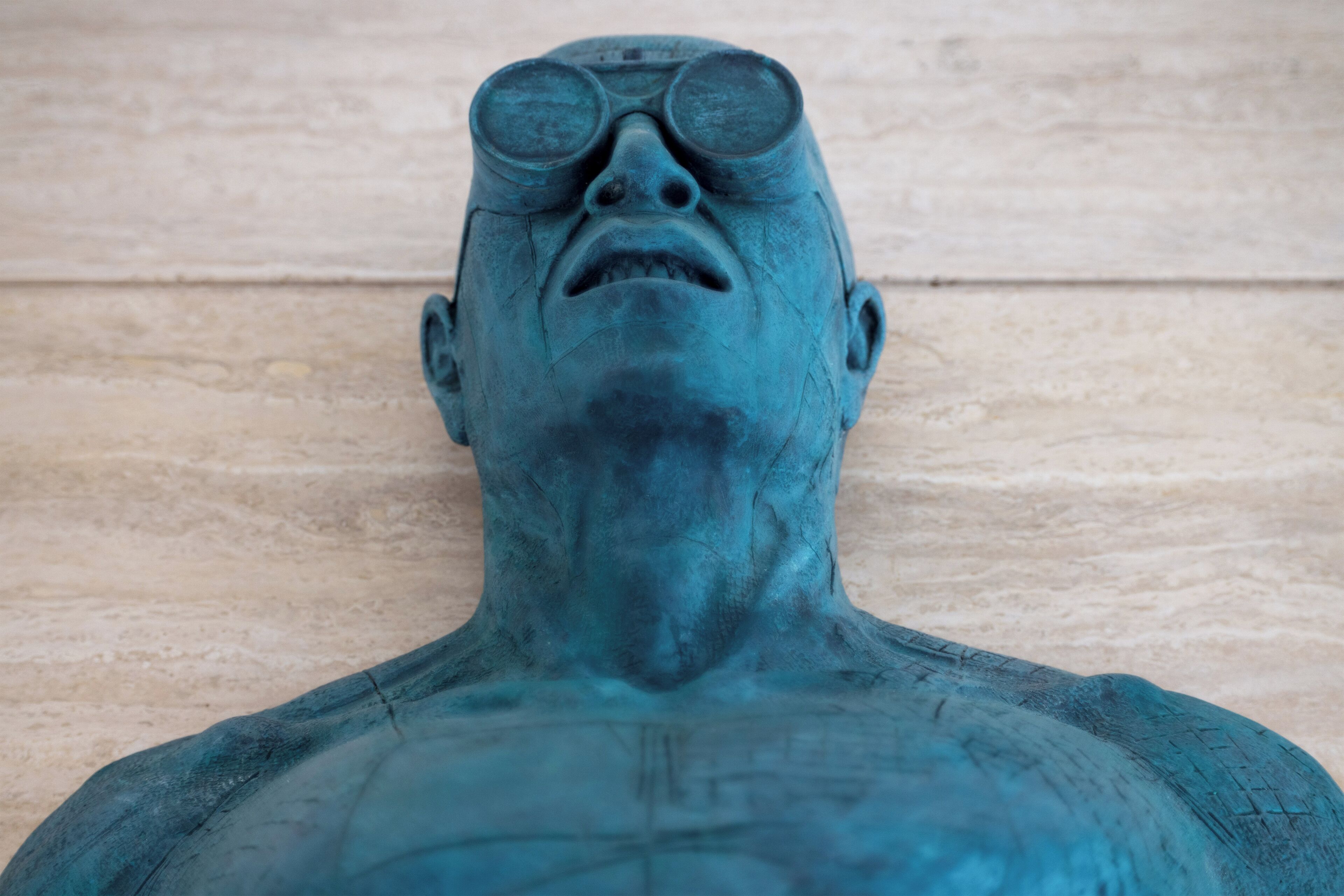 Una scultura raffigurante una persona dai toni blu, su uno sfondo di legno chiaro.