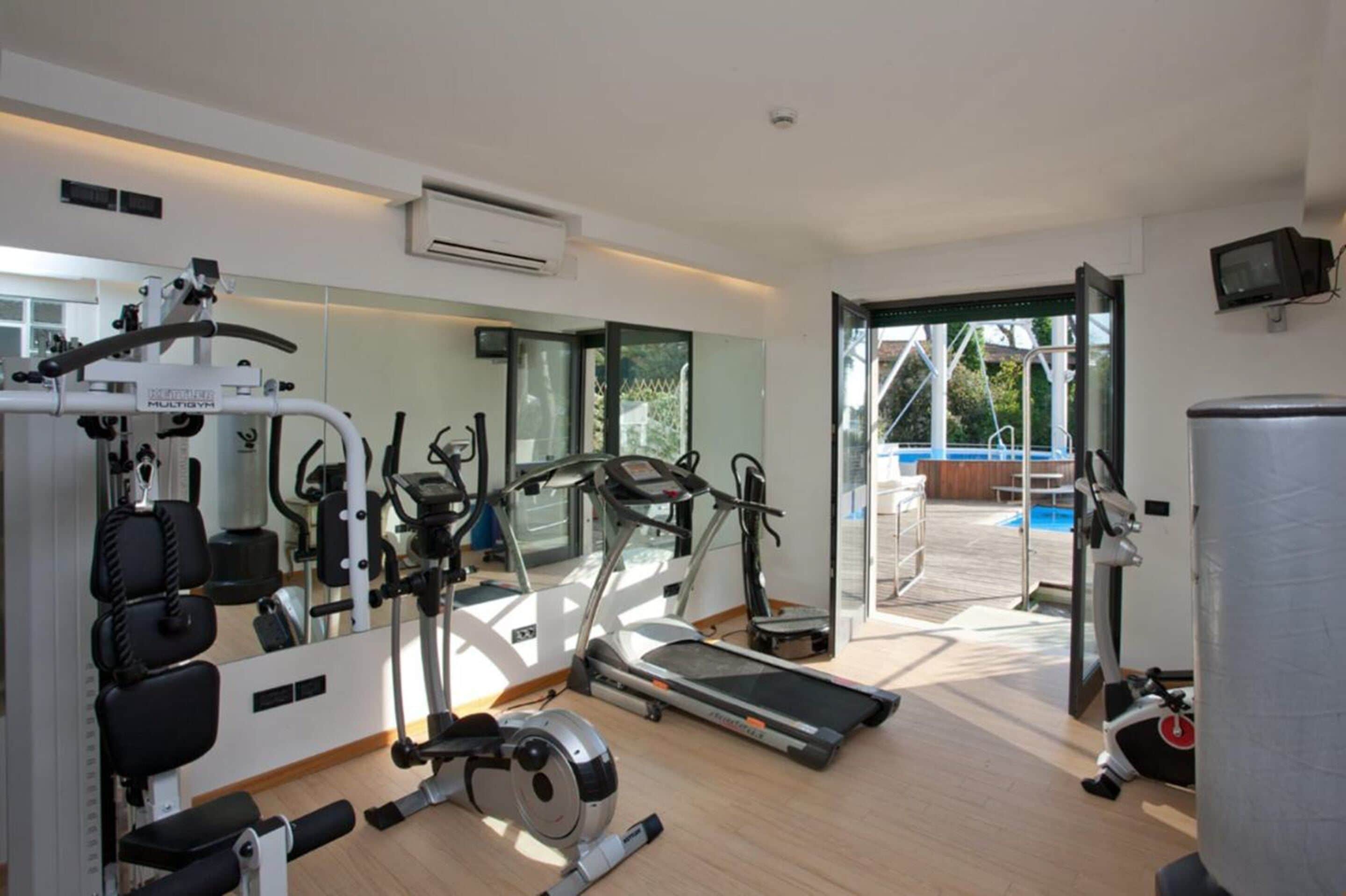A modern gym with cardio machines, a weight bench, and a large mirror.