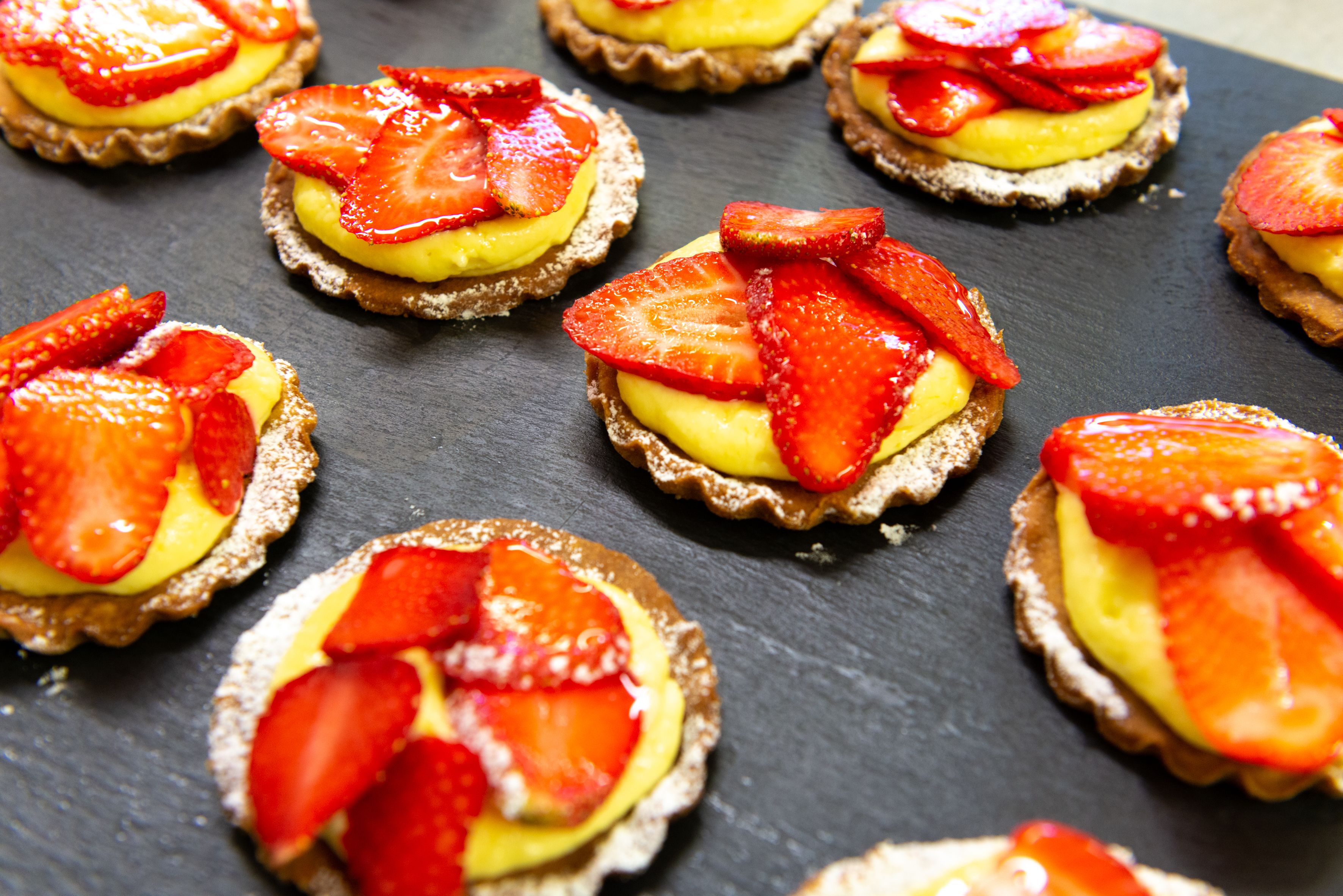 Eine Schieferplatte mit verschiedenen Törtchen, belegt mit Erdbeeren und einer gelben Füllung.