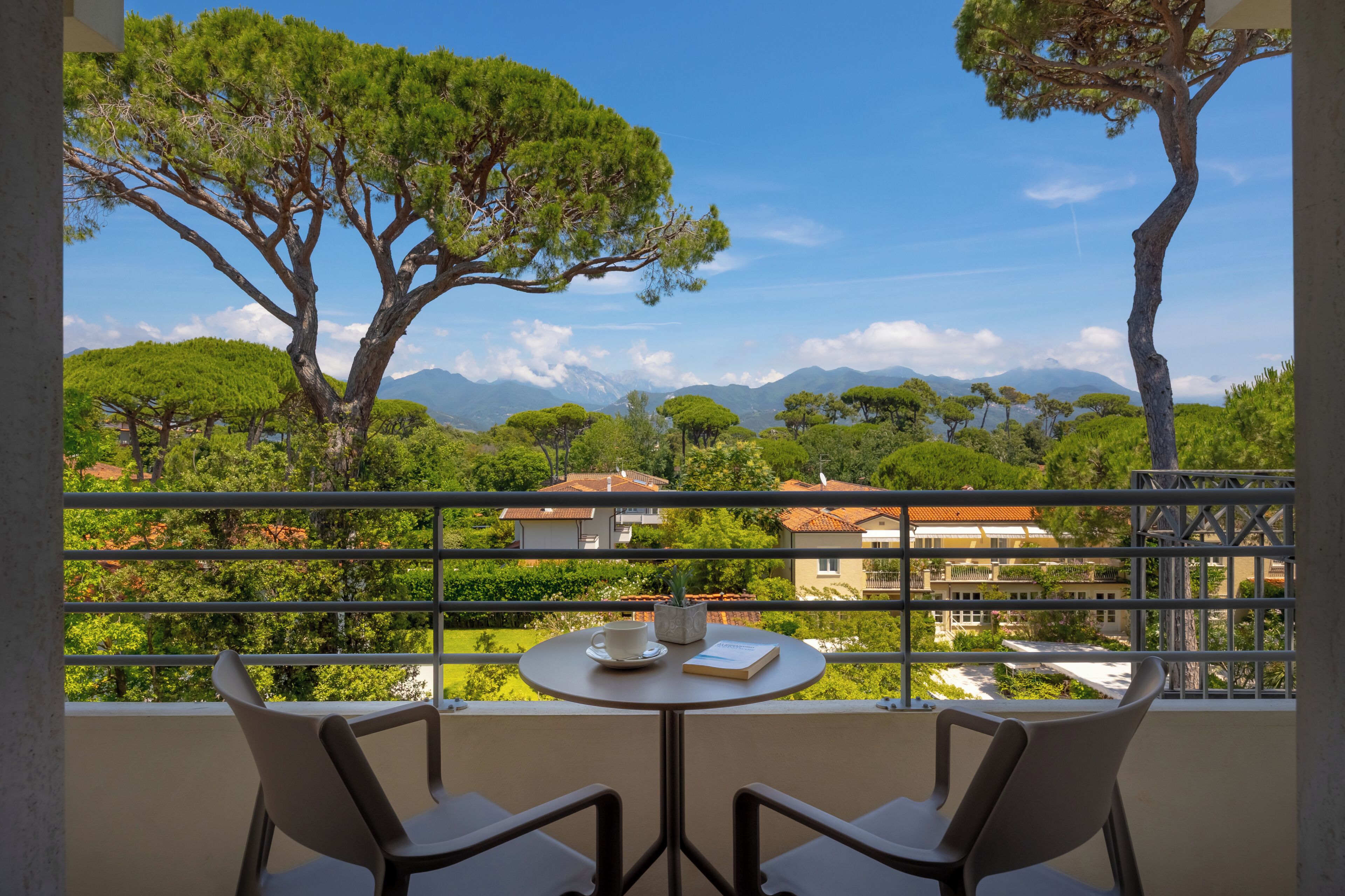 A balcony with a table, chairs, and a view of trees and buildings.