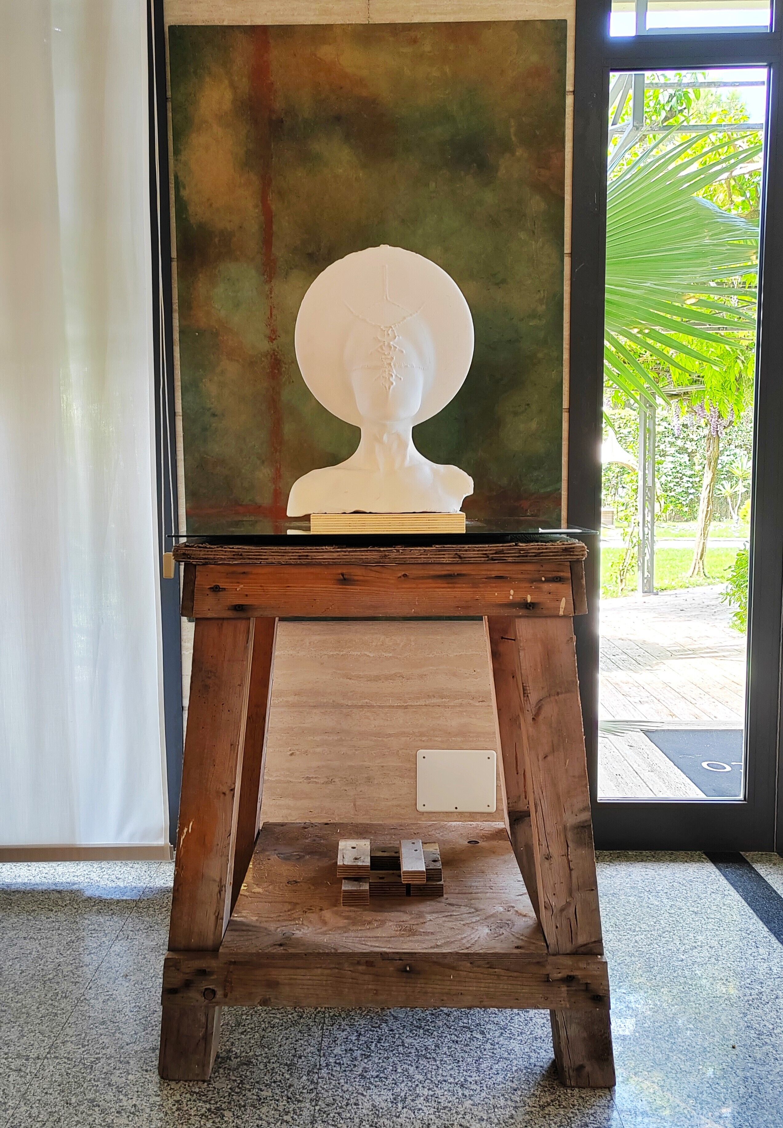 A wooden easel with a white bust sculpture on top, placed in front of a large abstract painting.