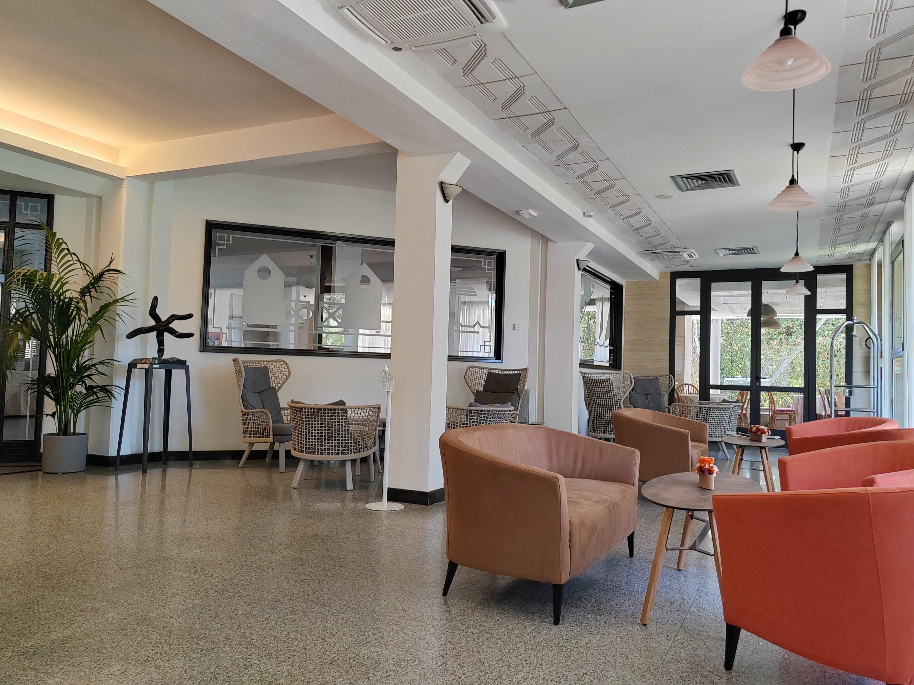 A spacious lobby with wicker furniture, a large window, and a ceiling with a geometric pattern.