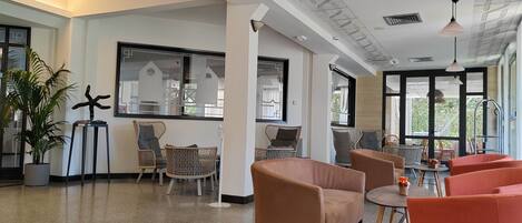 A spacious lobby with wicker furniture, a large window, and a ceiling with a geometric pattern.
