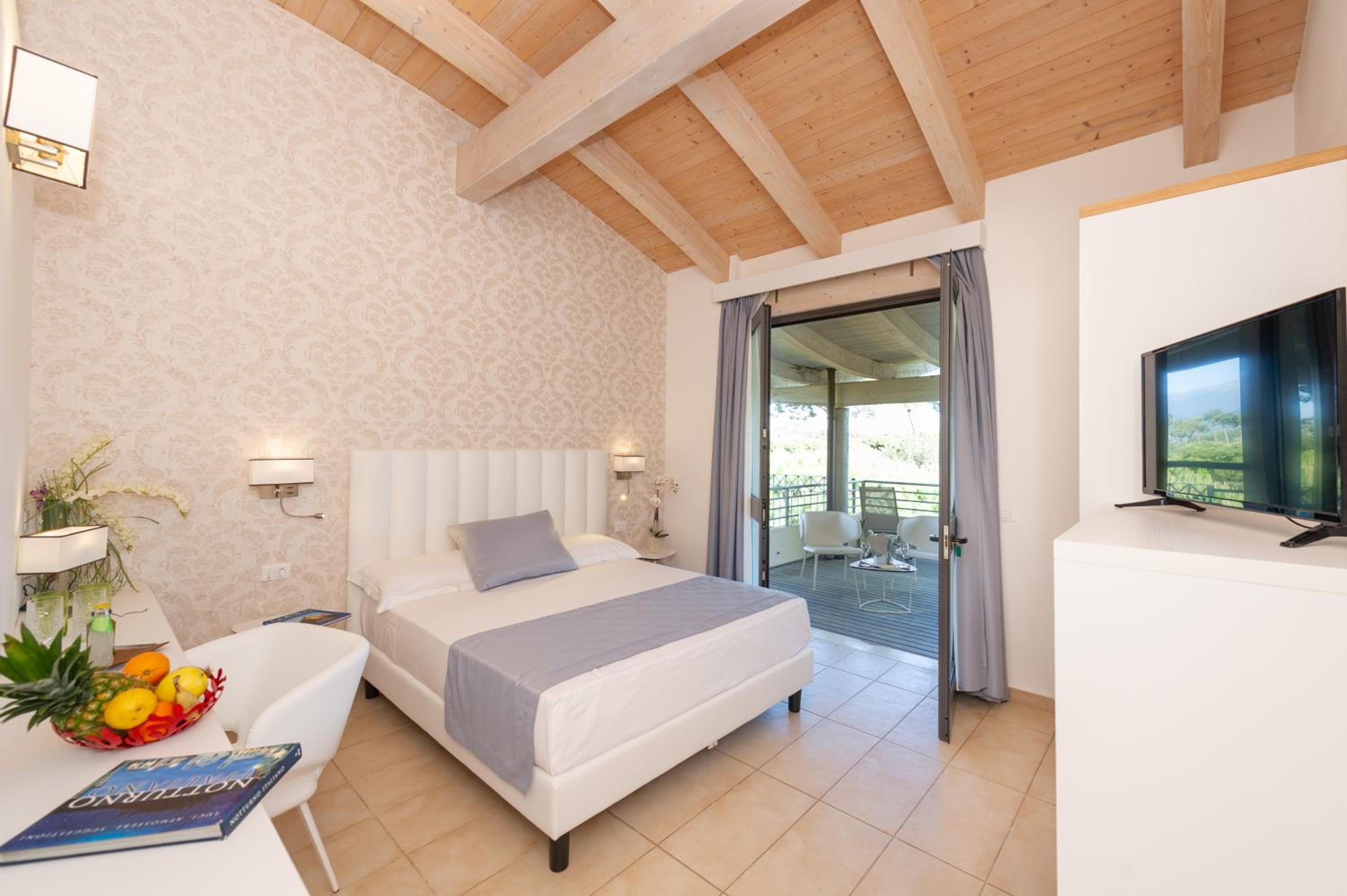 A bedroom with a bed, a TV, a dining table with fruit, and a balcony with a view.